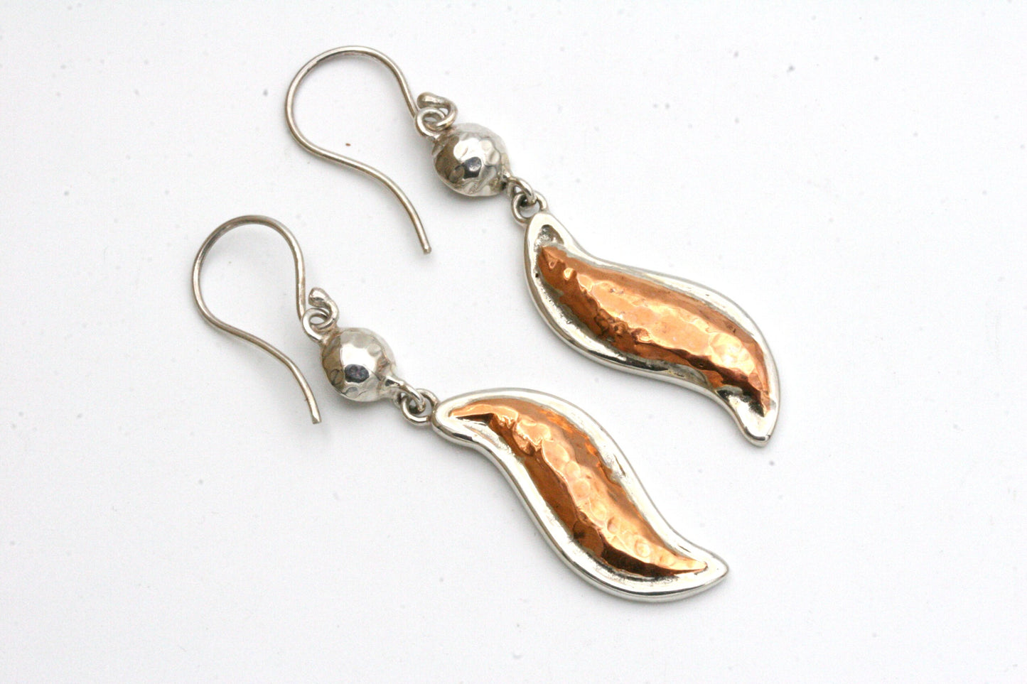 These beautiful wave shaped copper earrings are shiny and eye catching.
They feature hammered copper in the center with an outside bezel of solid sterling silver.
At the top of the earrings are hammered pillow beads in sterling silver.
All ready to dress up any outfit!
The earrings measure 2 inches from the top of the ear wire to the bottom and have sterling silver ear wires.