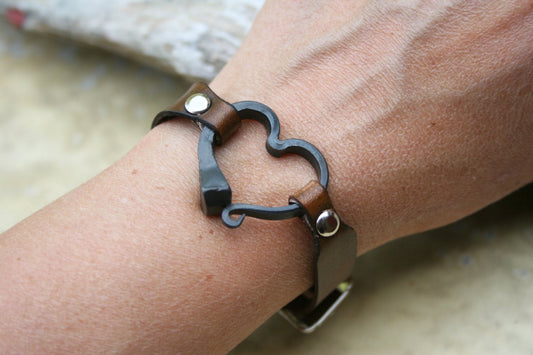 My Black smith made horse shoe nail bracelet is comfortable to wear and makes a great Iron anniversary gift or present for the horse lover in your family. 
The heart is held by a beautiful brown dyed leather band and the bracelet is adjustable. Each heart is handmade by me in a coal forge, shaped on the anvil, brushed, and finished with wax to prevent rusting and add shine.....a one of a kind piece of Art.