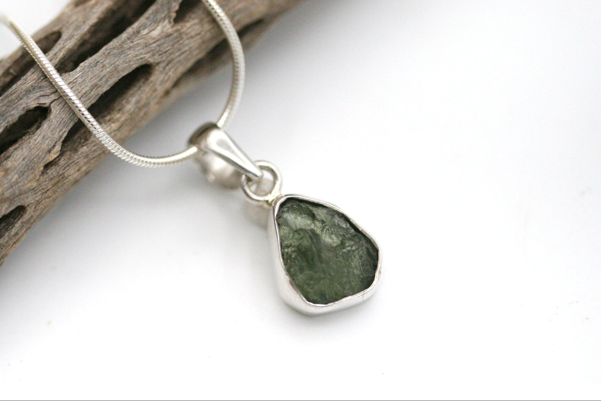 Green stone pendant on a silver chain against a white background
