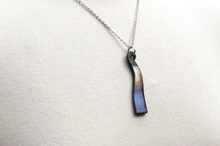 iron wave necklace features a pendant with rainbow color heat treatment. the pendant measures about 2 inches tall and has a vertical wave shape. Hunf from a stainless steel chain.