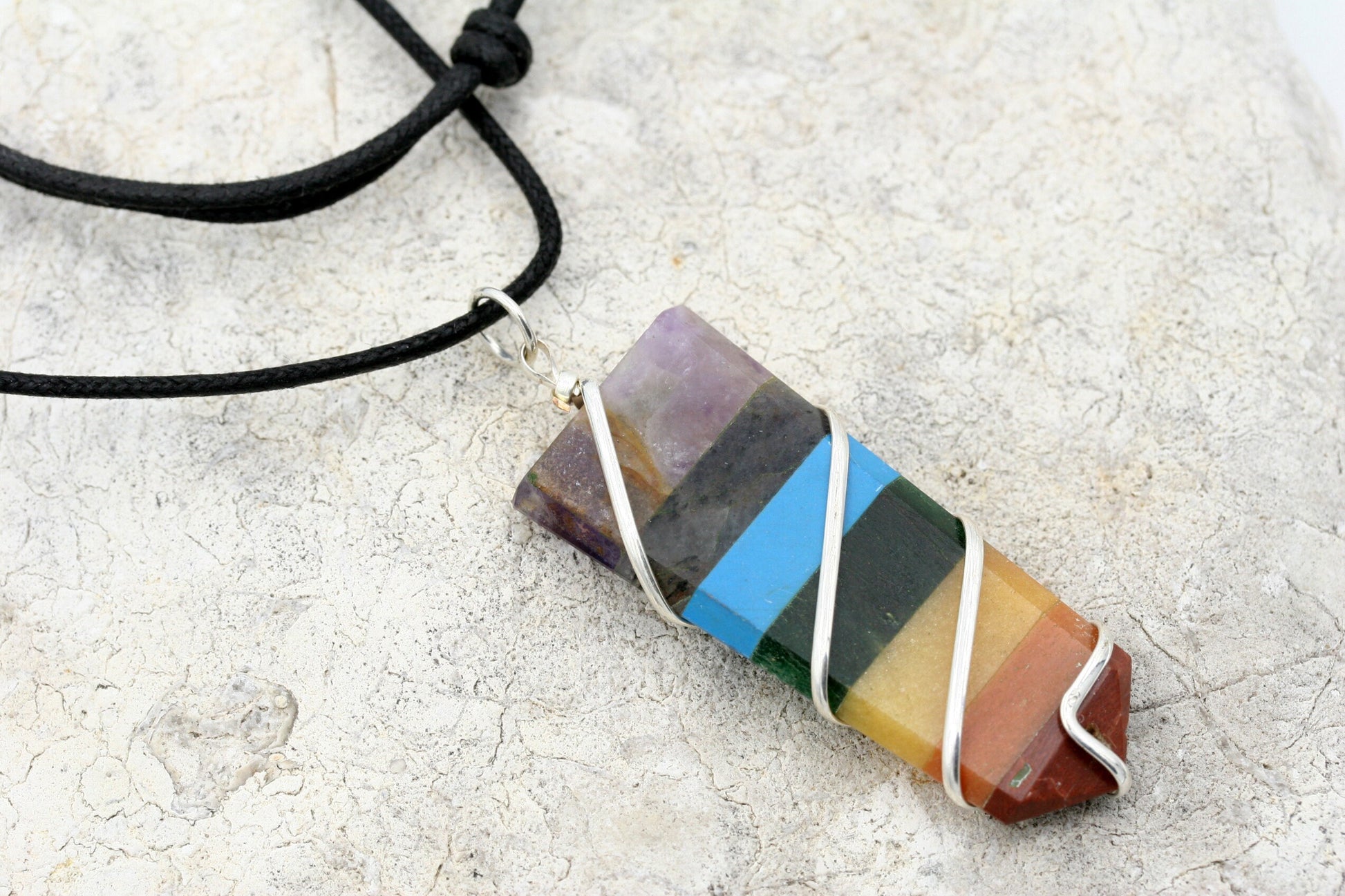Beautiful seven chakra gemstone pendant wrapped in sterling silver plated wire on a adjustable length waxed cotton cord.
The necklace is adjustable from 26 inches down to 15 inches with a sliding knots.

The pendant measures approximately 1/2" inch wide, 2 1/4" inch long and includes (from top to bottom) the stones Amethyst, Labradorite, Turquoise, Green Aventurine, Yellow Quartz, Orange Aventurine, and Red Jasper.