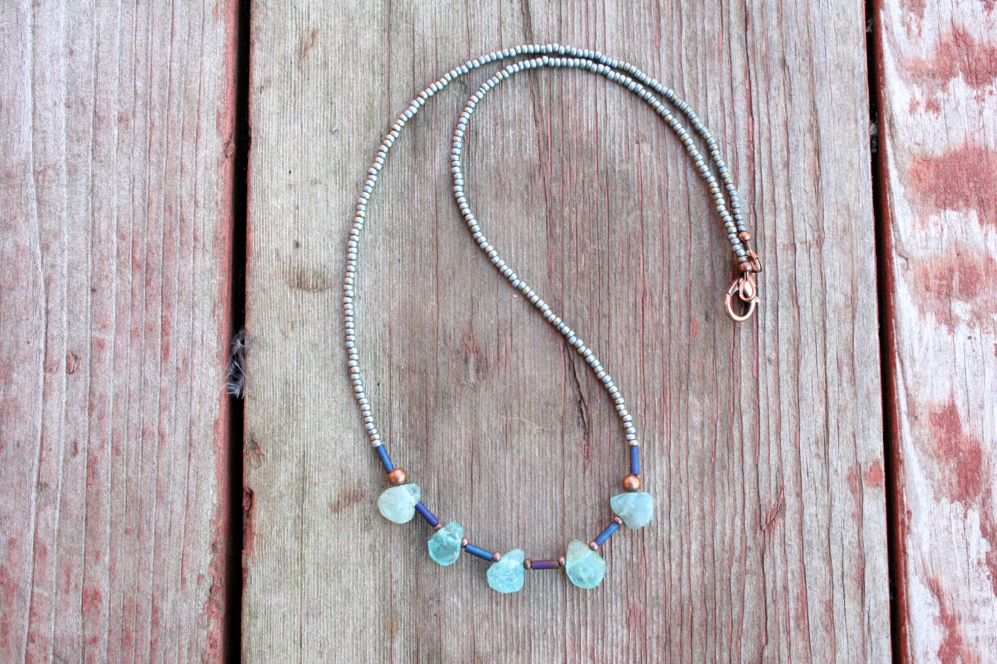 Genuine raw aquamarine teardrop beads with Japanese seed bead accents. Elegant and eye-catching, day and night!

The necklace measures 18 inches long and is finished off with an antiqued copper lobster clasp.