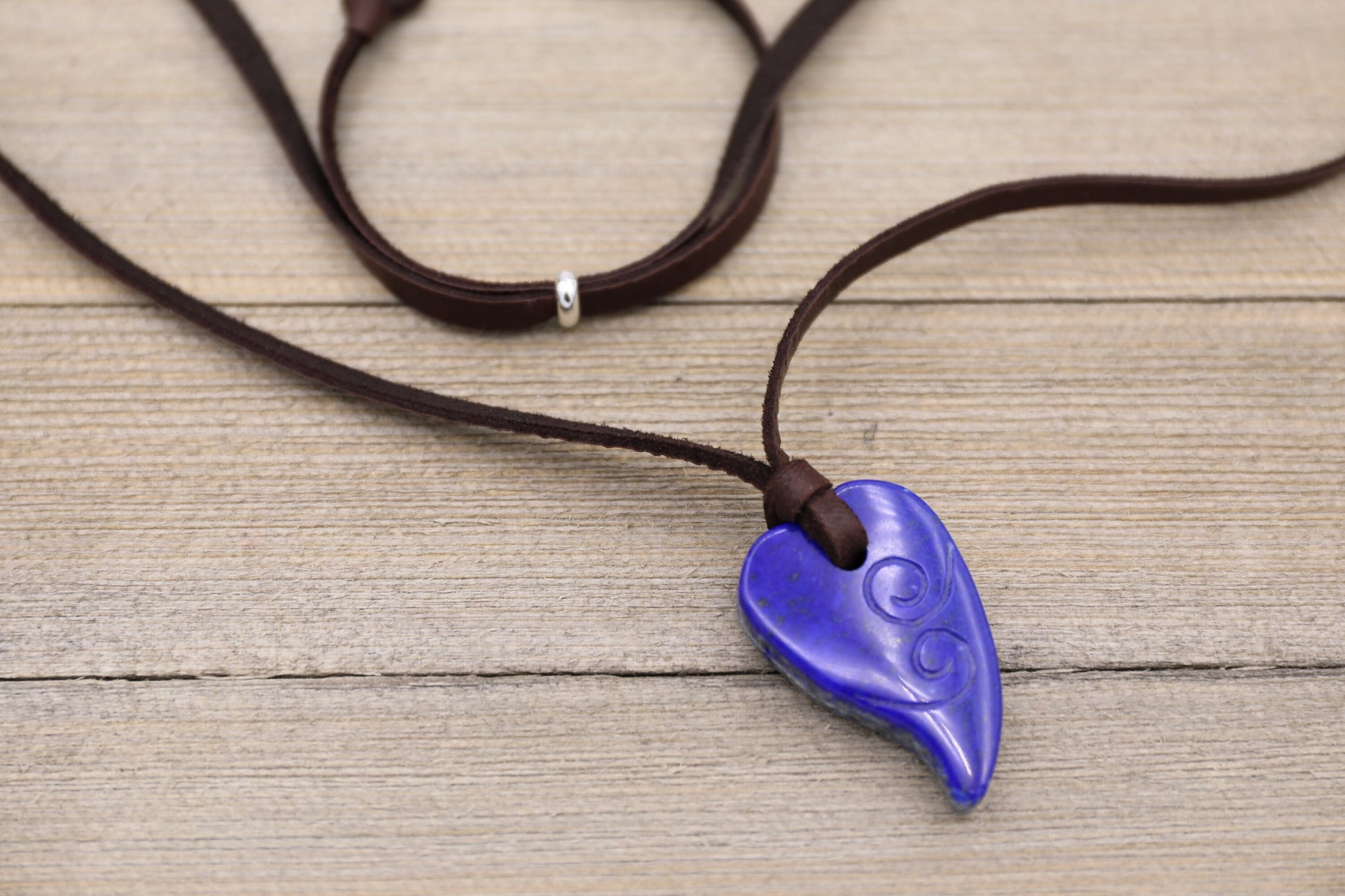 This beautiful necklace features a Lapis Lazuli heart pendant.

The heart is hand carved with delicate spirals on both sides.

This necklace hangs from a soft deerskin leather cord... adjustable in length from 30 inches long down to a choker with the sliding bead on the back. You can choose from either dark brown or tan leather when ordering.

The heart pendant measures 1 1/2 inches tall and 1 inch wide. This makes a truly beautiful and unique gift.