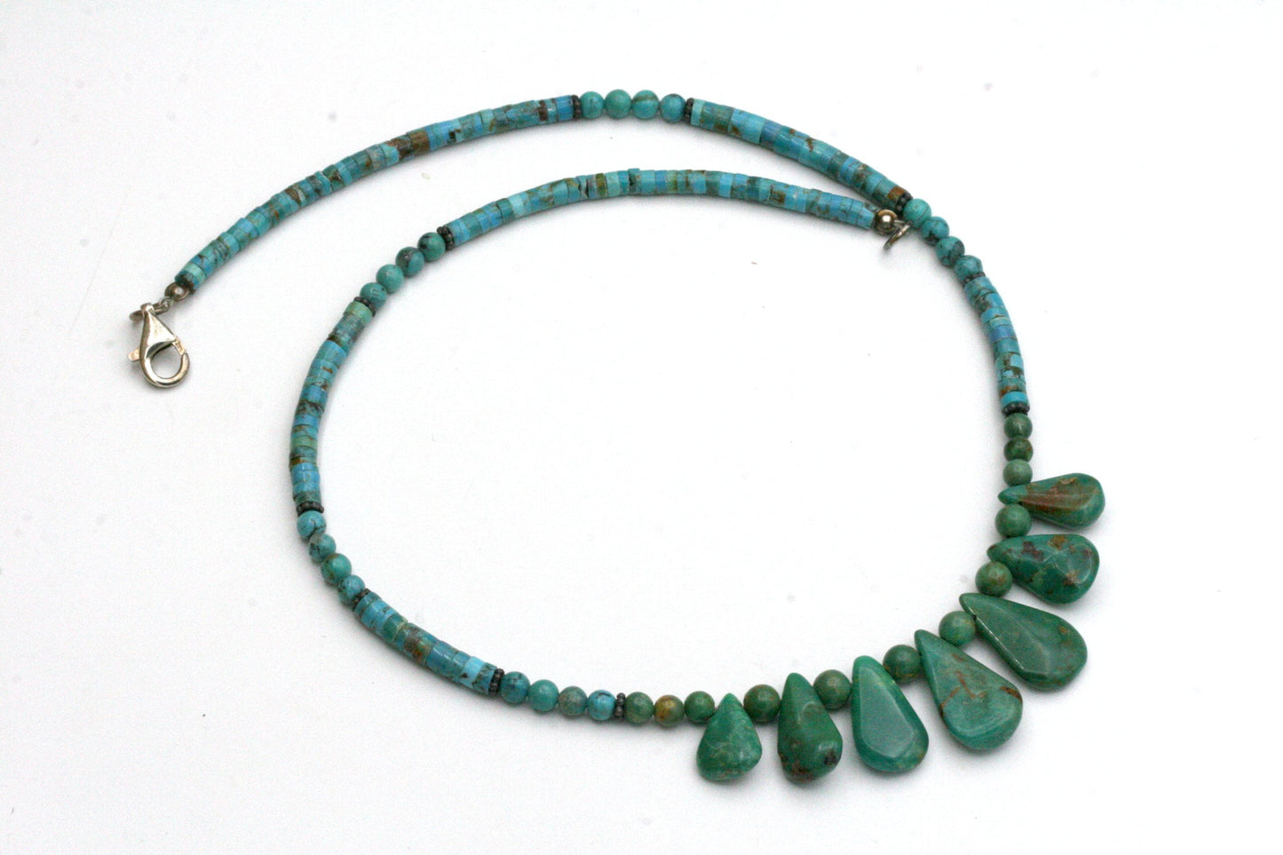 A turquoise necklace with a teardrop pendant design. The necklace is made of small round and tube shaped turquoise beads and larger teardrop-shaped turquoise stones. 