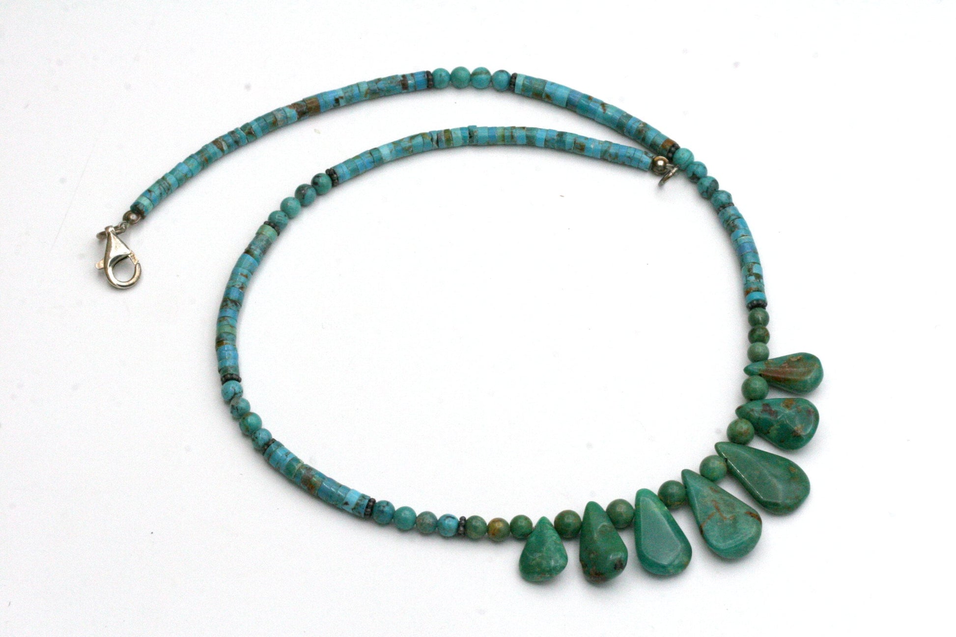 A turquoise necklace with a teardrop pendant design. The necklace is made of small round and tube shaped turquoise beads and larger teardrop-shaped turquoise stones. 